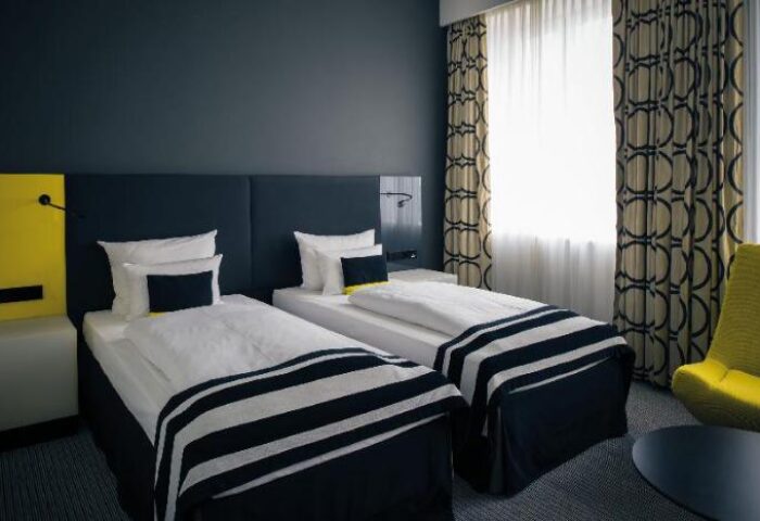 Vienna House Andel’s Berlin gay-friendly hotel room with twin beds. Pet-friendly stay. Modern design with black, white, and yellow accents.