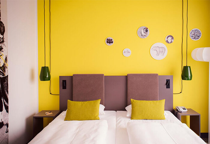Vienna House Easy Berlin room. Gay-friendly hotel with twin beds, yellow wall, bear art. Modern design for LGBTQ+ travelers in Berlin.
