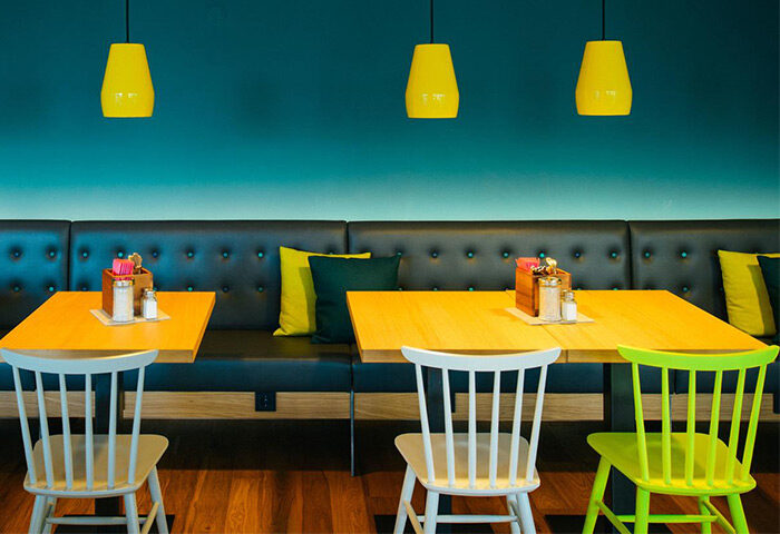 Vienna House Easy Berlin's gay-friendly hotel restaurant. Interior view with tables, chairs, yellow lamps, and a blue wall. Modern design.
