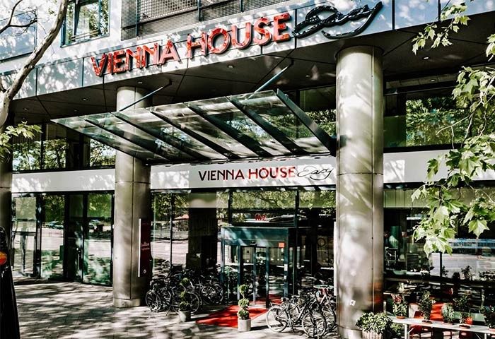 Vienna House Easy Berlin entrance. Gay-friendly hotel with modern architecture, glass canopy, and bicycles parked outside. Berlin gay travel.