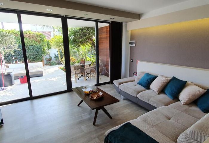 Villa Adler Gay Men Only lounge area with a view to the garden. Gay-friendly hotel interior with sofa, table, and outdoor seating.