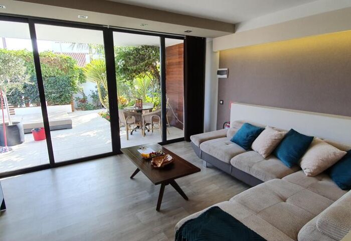 Villa Adler Gay Men Only lounge area with a view to the garden. Gay-friendly hotel interior with sofa, table, and outdoor seating.