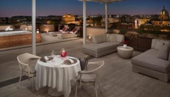 Villa Agrippina Gran Melia gay-friendly hotel rooftop. Dining table, lounge chairs, jacuzzi, and Rome city view. Luxury gay travel.