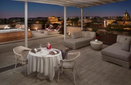 Villa Agrippina Gran Melia gay-friendly hotel rooftop. Dining table, lounge chairs, jacuzzi, and Rome city view. Luxury gay travel.