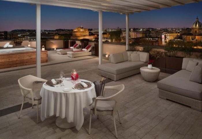 Villa Agrippina Gran Melia gay-friendly hotel rooftop. Dining table, lounge chairs, jacuzzi, and Rome city view. Luxury gay travel.