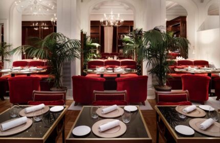 Villa Agrippina Gran Melia's elegant dining room. Tables are set with red chairs, plants, and chandeliers. Gay-friendly hotel decor.