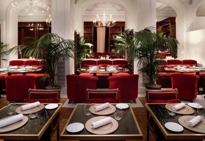 Villa Agrippina Gran Melia's elegant dining room. Tables are set with red chairs, plants, and chandeliers. Gay-friendly hotel decor.