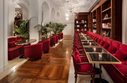Villa Agrippina Gran Melia's interior. Gay-friendly hotel lounge with red velvet seating, tables, and bookshelves. Elegant design.