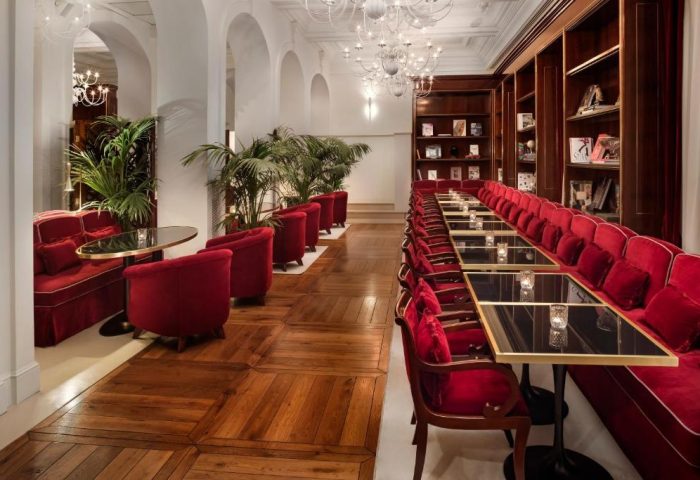 Villa Agrippina Gran Melia's interior. Gay-friendly hotel lounge with red velvet seating, tables, and bookshelves. Elegant design.