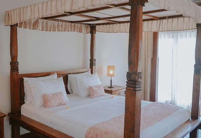 Villa Kresna Boutique and Suites gay-friendly hotel room. Four-poster bed with white linens, soft lighting, and elegant decor. Relaxing space.
