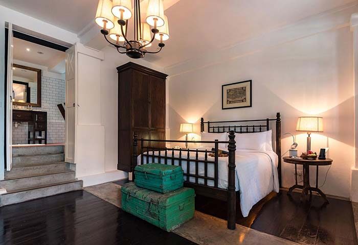 Villa Samadhi Singapore bedroom. Gay-friendly hotel room with bed, vintage trunks, wardrobe, and chandelier. Luxury travel for gay men.
