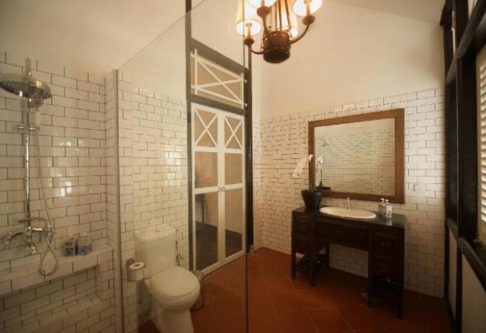 Villa Samadhi Singapore bathroom. Shower, toilet, and sink. The gay-friendly hotel features vintage design, white brick tiles and terracotta floor.
