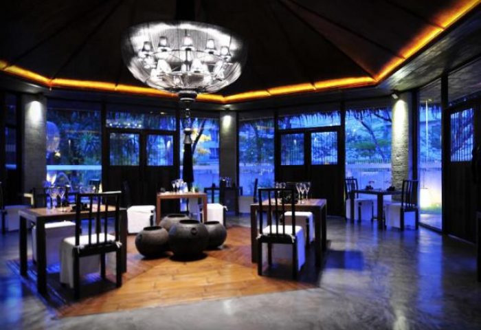 Villa Samadhi by Samadhi, a gay-friendly hotel. Interior view of the dining area with tables, chairs, and a chandelier. Night scene.