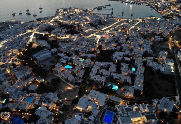 Villa Varnali Small Boutique, a gay-friendly hotel. Aerial view of Mykonos town at night, showing illuminated buildings and pools.