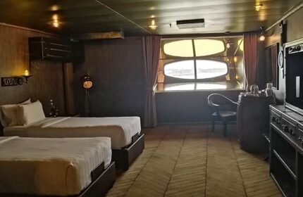 Vintage Luxury Yacht Hotel gay-friendly room. Two beds, barrel table, and porthole window. Unique stay for gay men travelers.