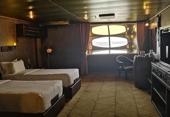 Vintage Luxury Yacht Hotel gay-friendly room. Two beds, barrel table, and porthole window. Unique stay for gay men travelers.