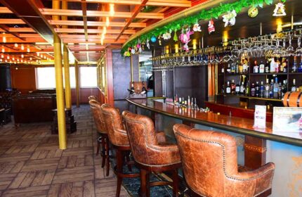 Bar area at Gay-Friendly Vintage Luxury Yacht Hotel. Leather bar stools line the counter. Bottles and glasses are displayed behind the bar.
