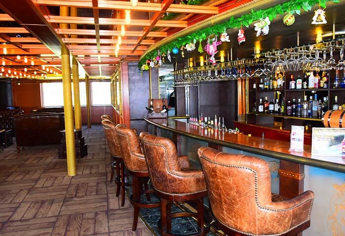 Bar area at Gay-Friendly Vintage Luxury Yacht Hotel. Leather bar stools line the counter. Bottles and glasses are displayed behind the bar.
