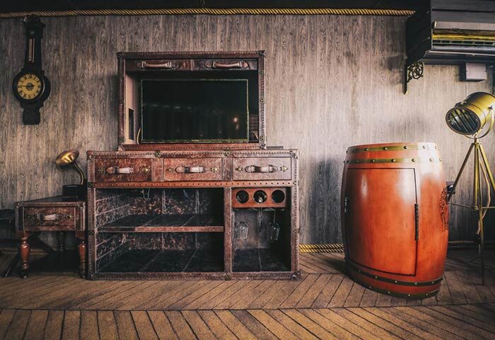 Vintage Luxury Yacht Hotel room decor. Leather trunk-style furniture, barrel bar, clock, and spotlight. Gay-friendly hotel design.