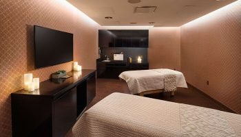 Spa room at gay-friendly Virgin Hotels Las Vegas, Curio Collection by Hilton. Two massage beds, TV, candles, and sink area.