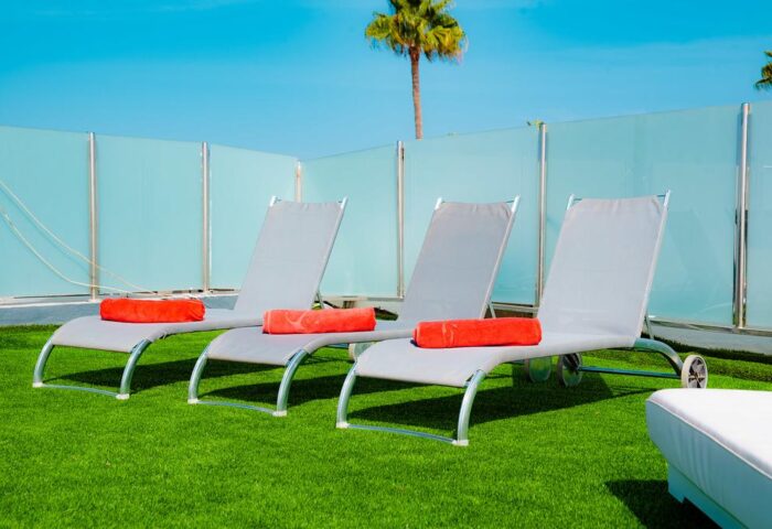 Vista Bonita Gay Resort: Sun loungers with towels on green turf. Relax at this gay-friendly hotel. Palm tree and blue sky in background.