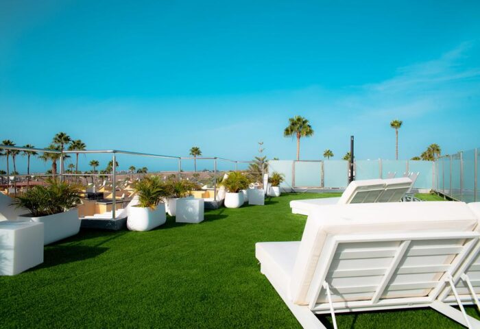 Vista Bonita Gay Resort rooftop. White loungers, planters, and green turf under a clear blue sky. Gay-friendly hotel for men's travel.