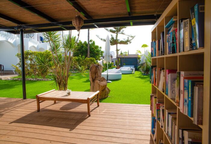 Vista Bonita Gay Resort's outdoor lounge area. Bookshelf, wooden table, and lawn with sunbeds. A gay-friendly hotel for a relaxing vacation.