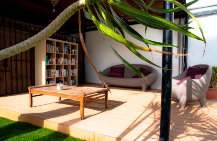 Vista Bonita Gay Resort's relaxing outdoor lounge area. Gay-friendly hotel with a bookshelf, couch, chair, and coffee table on a wooden deck.