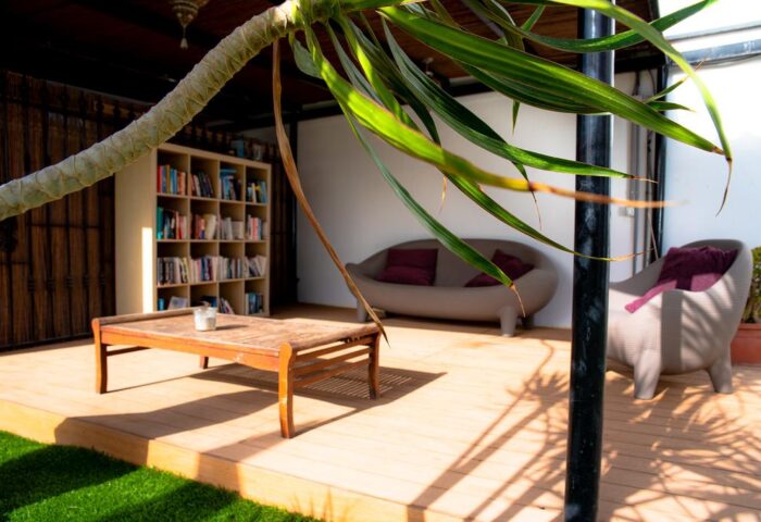 Vista Bonita Gay Resort's relaxing outdoor lounge area. Gay-friendly hotel with a bookshelf, couch, chair, and coffee table on a wooden deck.