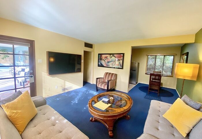 Living area at Vista Grande Resort, a gay men's resort. Room with couches, TV, table, and access to the pool. Gay-friendly hotel.