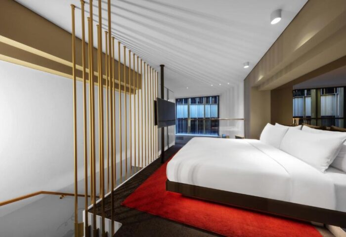 W Amsterdam gay-friendly hotel room. Modern design with gold accents, red rug, and large bed. A luxurious stay for gay travelers in Amsterdam.