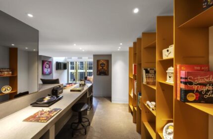 W Amsterdam gay-friendly hotel room. A long counter with a record player and stool, and a yellow bookshelf filled with books and decor.
