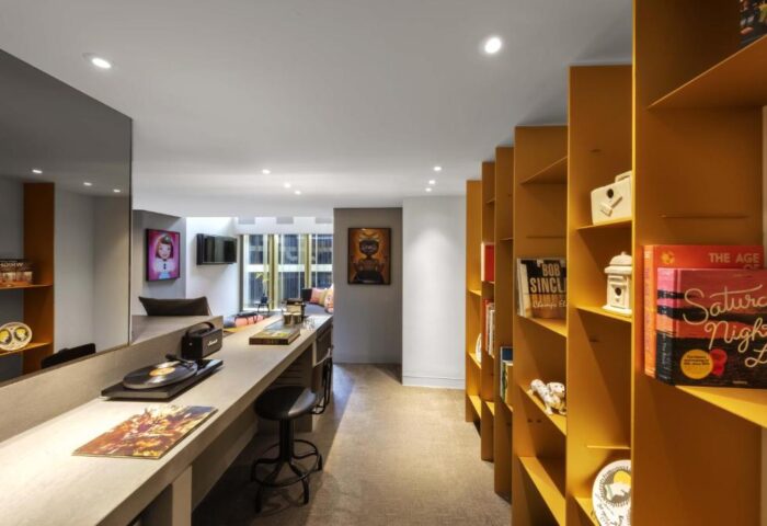 W Amsterdam gay-friendly hotel room. A long counter with a record player and stool, and a yellow bookshelf filled with books and decor.