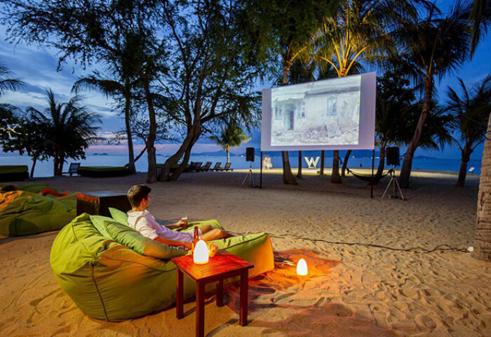 Gay-friendly W Koh Samui hotel beach cinema. Man relaxing on a beanbag chair watching a movie. Pet-friendly resort.