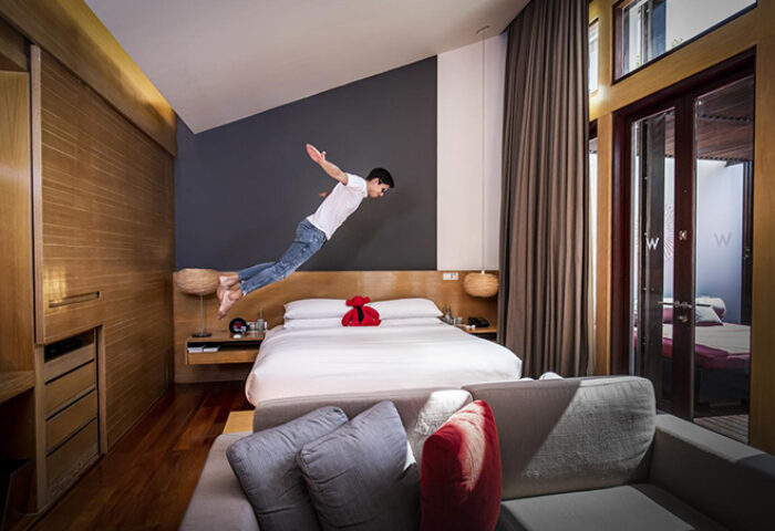 Man jumping over bed in W Koh Samui's gay-friendly hotel room. Pet-friendly resort offers luxury, comfort, and fun for gay travelers.