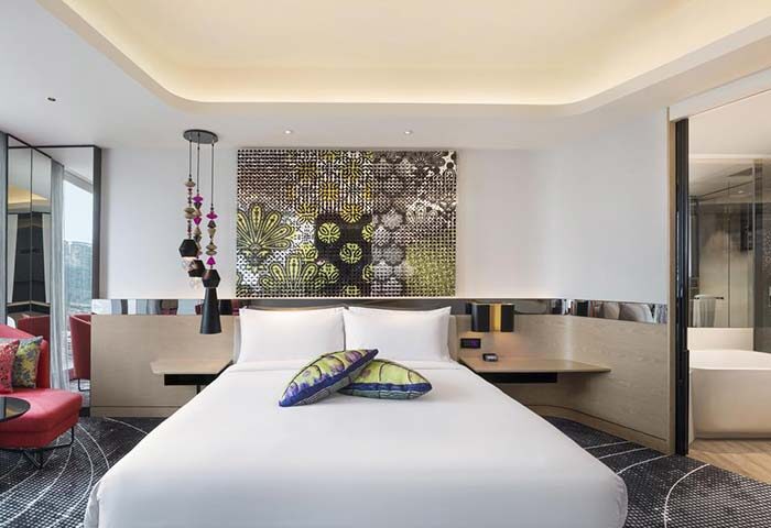 W Kuala Lumpur gay-friendly hotel room. King bed with colorful pillows, art above the bed, and a peek into the bathroom. Modern design.