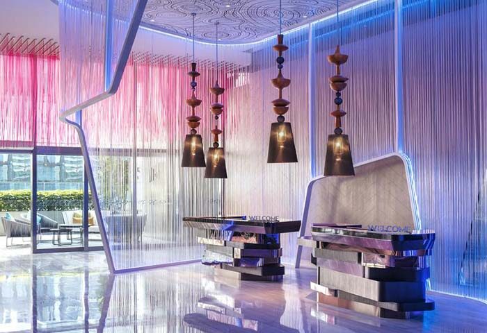 W Kuala Lumpur gay-friendly hotel lobby. Modern design with hanging lights, reception desk, and colorful lighting. Stylish travel for gay men.