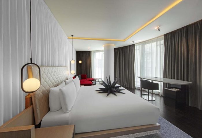 W London Leicester Square gay-friendly hotel room. Pet-friendly room with white bedding, modern lighting, and a red sofa. Luxury design.