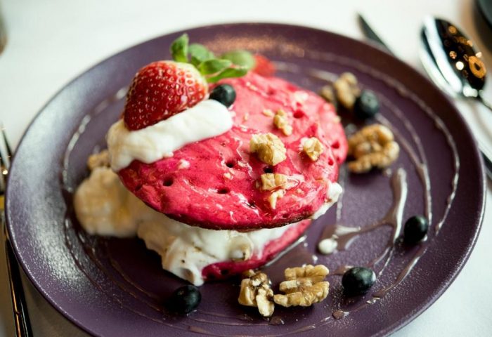 W London Leicester Square: Pink pancakes with cream, strawberry, blueberries and walnuts on a purple plate, gay-friendly, pet-friendly hotel.