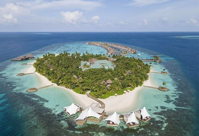 Aerial view of W Maldives, a gay-friendly hotel. Tropical island with palm trees, white sand beaches, overwater bungalows. Perfect for LGBTQ+ travel.