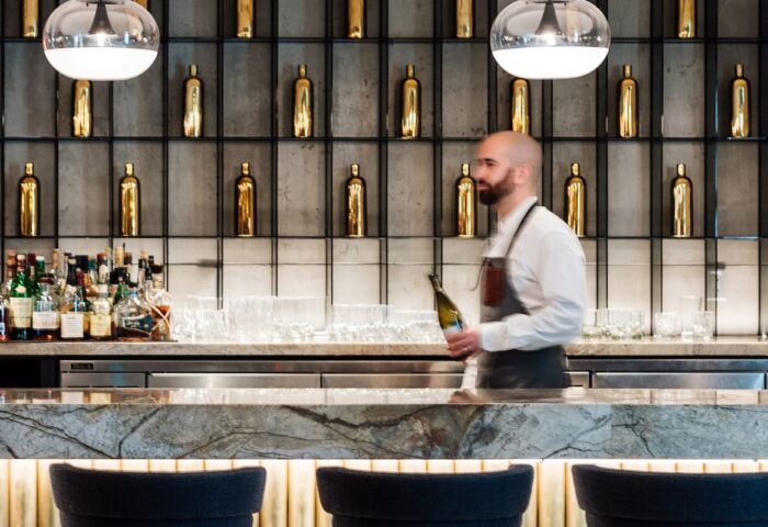 Bar at W Montréal, a gay-friendly hotel. Bartender holding a bottle stands in front of a marble bar with bottles and glasses.