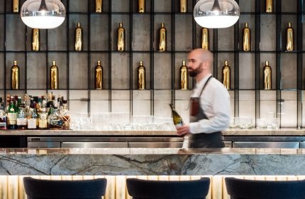 Bar at W Montréal, a gay-friendly hotel. Bartender holding a bottle stands in front of a marble bar with bottles and glasses.