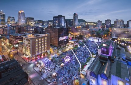 Night view of W Montreal, a gay-friendly hotel, overlooking a crowded outdoor event in the city. Montreal's skyline is visible.