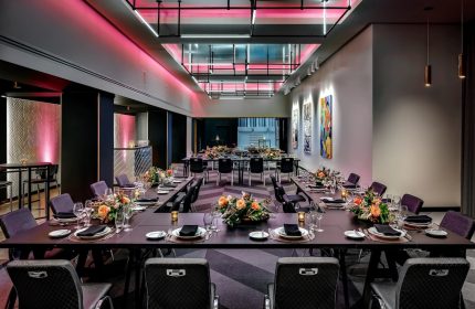 W Montréal gay-friendly hotel event space. Long tables are set with flowers, glasses, and plates. Pink lighting adds a vibrant touch.