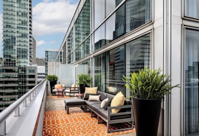 W Montréal gay-friendly hotel, outdoor terrace. Modern furniture, orange rug, plants. City view. Chic, stylish design. Urban retreat.