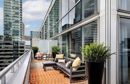 W Montréal gay-friendly hotel, outdoor terrace. Modern furniture, orange rug, plants. City view. Chic, stylish design. Urban retreat.