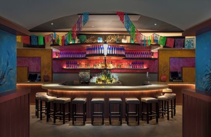 Bar at W New York - Times Square, a gay-friendly hotel. Colorful decor, bottles, and stools create an inviting atmosphere.