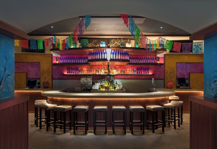 Bar at W New York - Times Square, a gay-friendly hotel. Colorful decor, bottles, and stools create an inviting atmosphere.