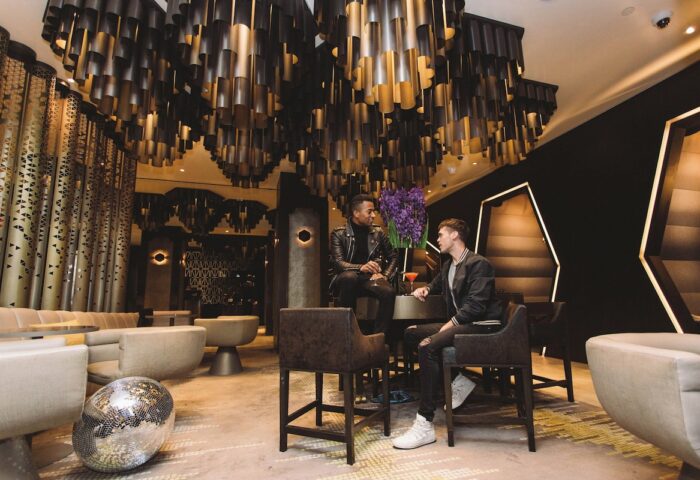 Gay-friendly W New York Times Square Hotel bar. Two men enjoy cocktails under a modern chandelier. Disco ball on the floor. NYC gay travel.