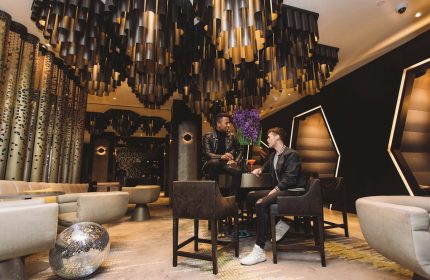 Gay-friendly W New York Times Square Hotel bar. Two men enjoy cocktails under a modern chandelier. Disco ball on the floor. NYC gay travel.